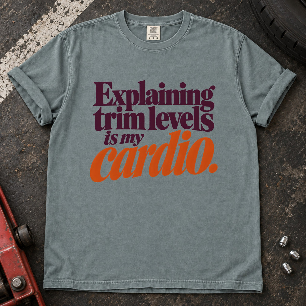 Bay T-shirt with burgundy and orange lettering reading 'Explaining trim levels is my cardio'.