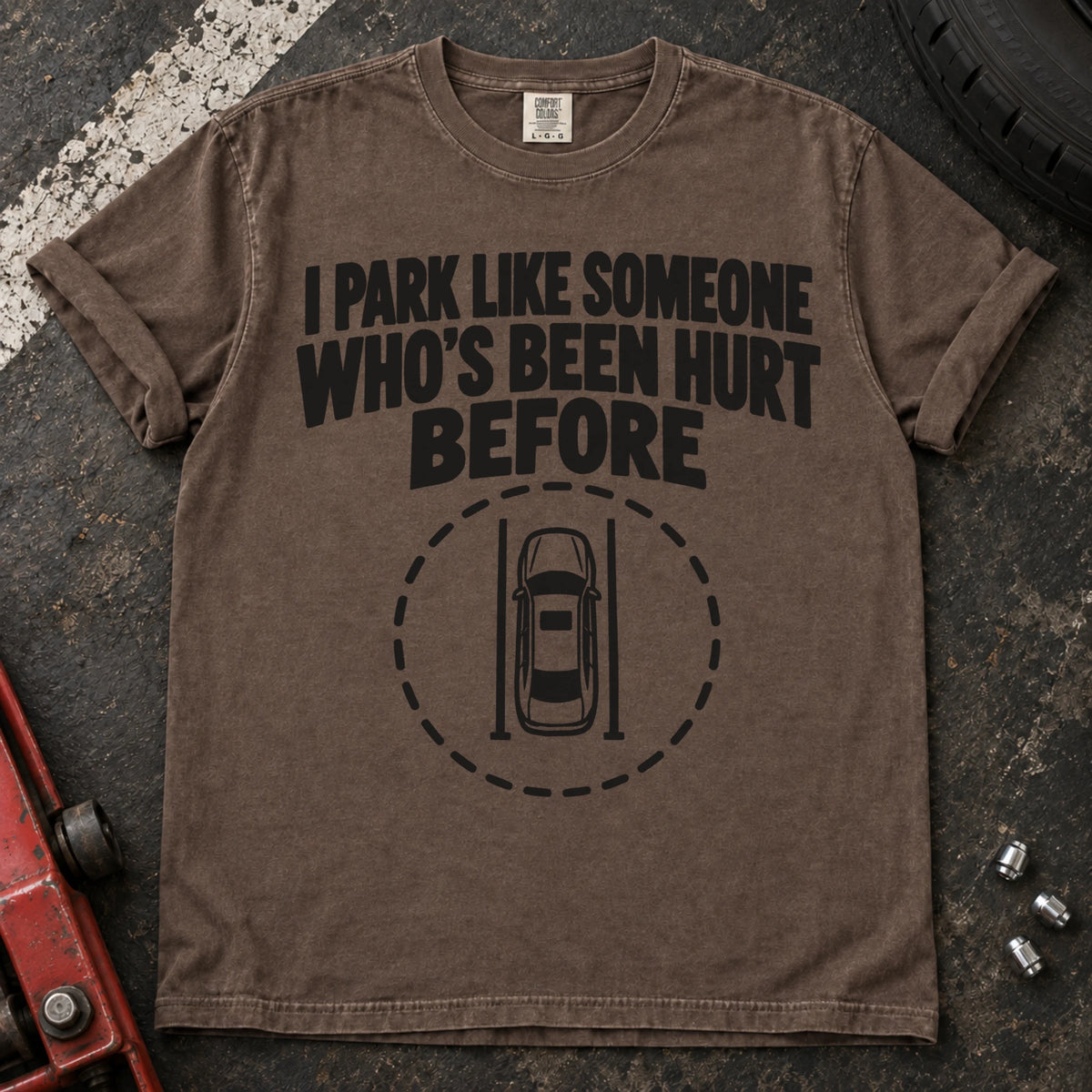 Espresso T-shirt showing an overhead car inside a dashed circle with 'I park like someone who's been hurt before'.