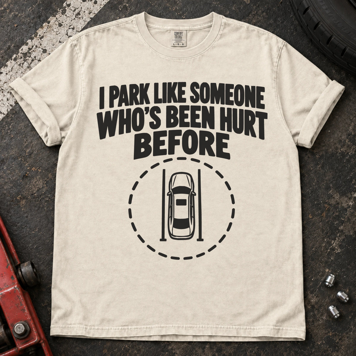 Ivory T-shirt showing an overhead car inside a dashed circle with 'I park like someone who's been hurt before'.
