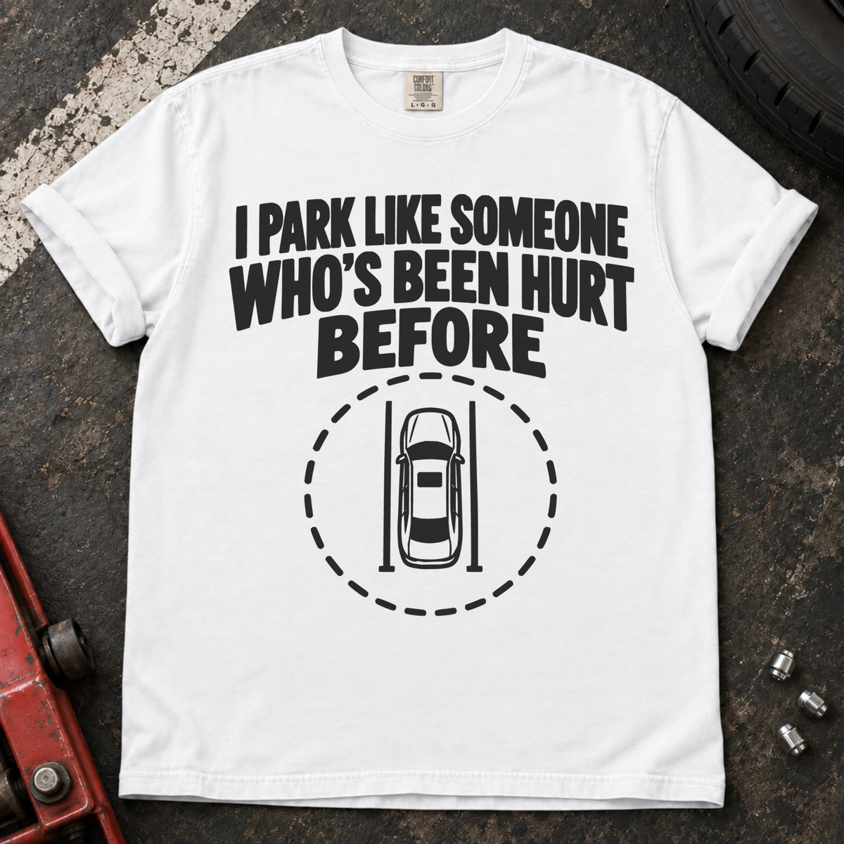 White T-shirt showing an overhead car inside a dashed circle with 'I park like someone who's been hurt before'.
