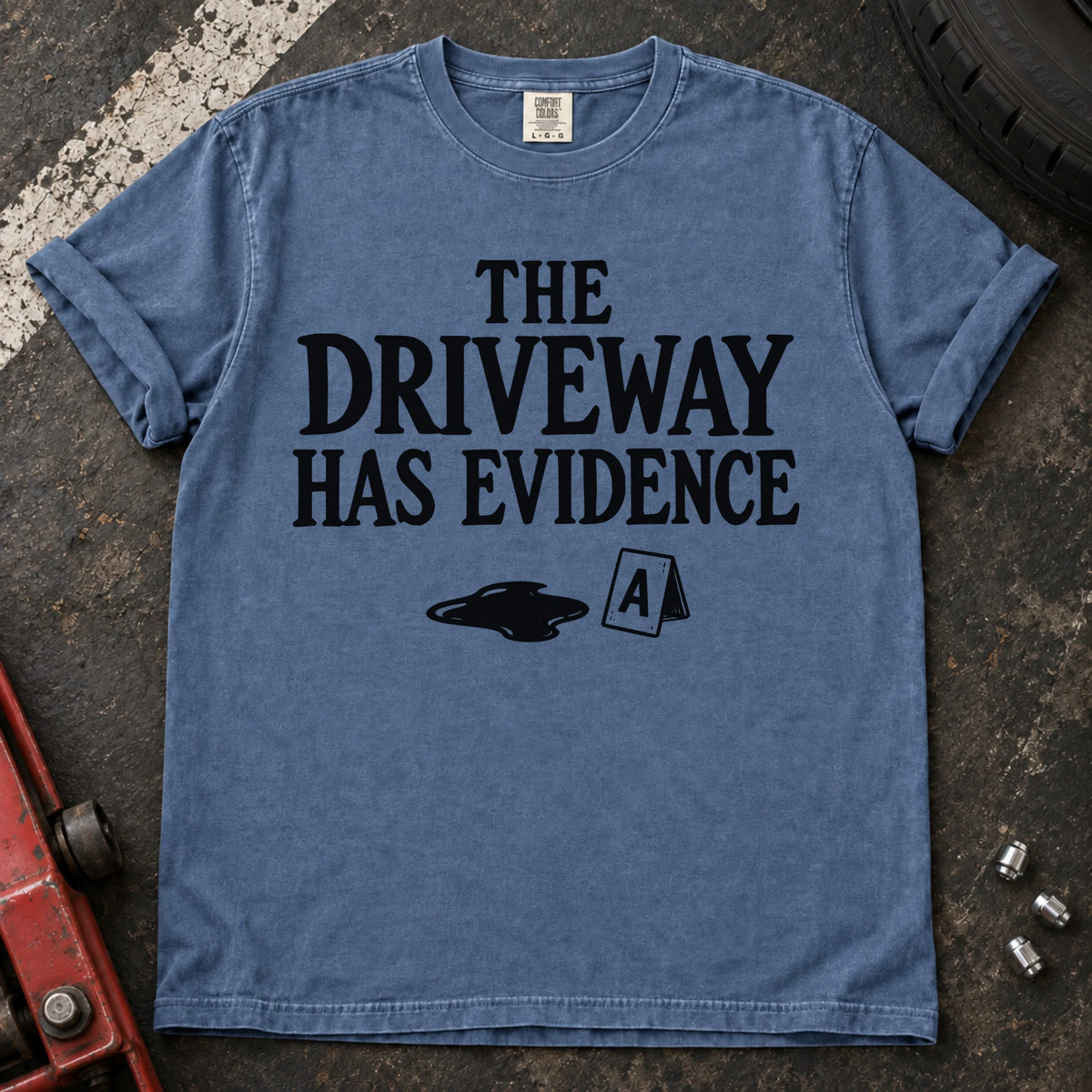 Blue Jean T-shirt showing an oil puddle and evidence marker beneath 'The driveway has evidence'.