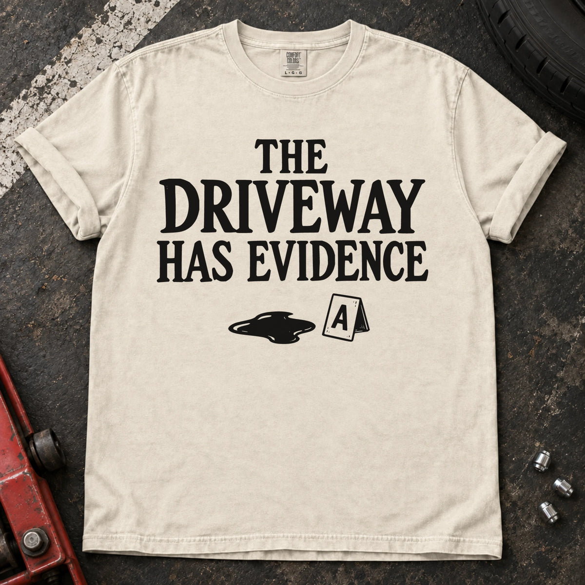 Ivory T-shirt showing an oil puddle and evidence marker beneath 'The driveway has evidence'.