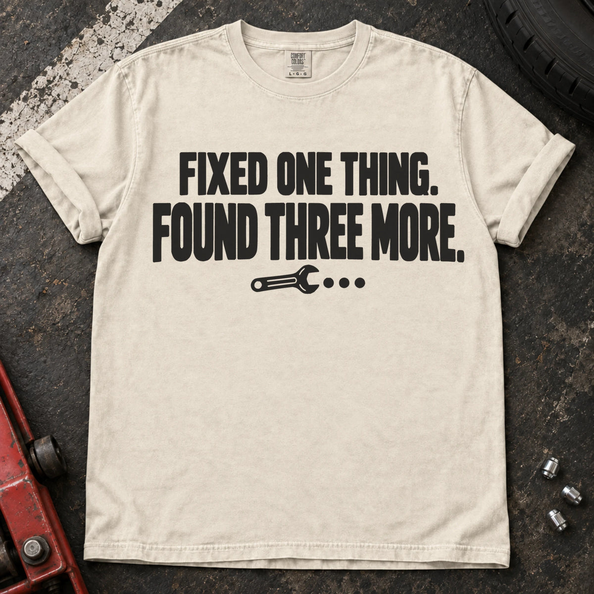 Ivory T-shirt reading 'Fixed one thing. Found three more' above a small wrench.