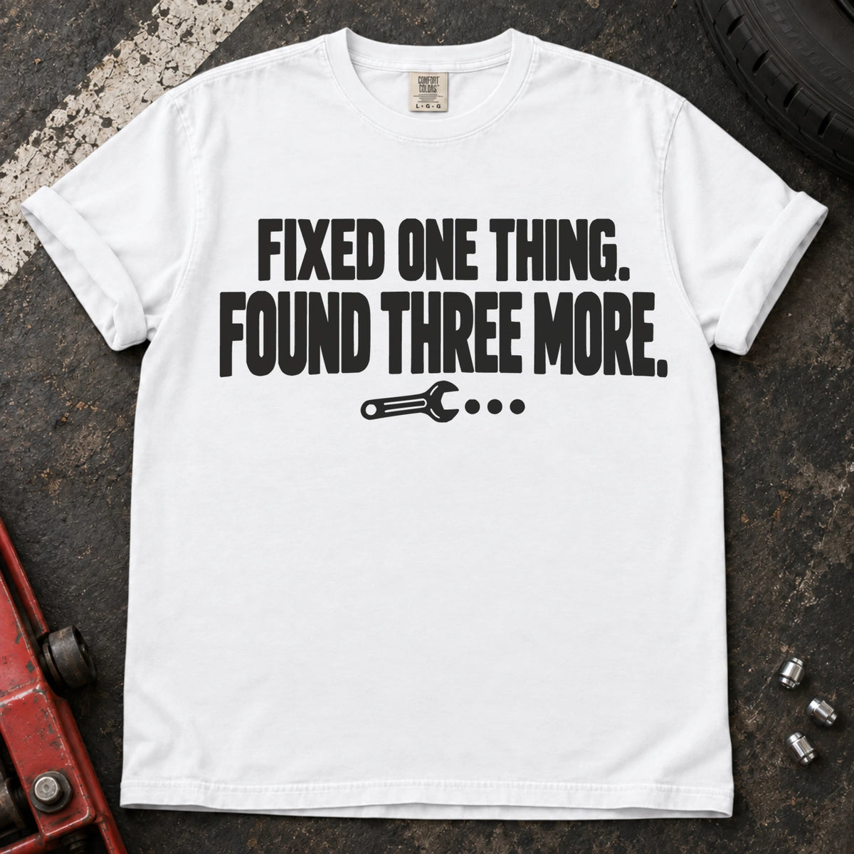White T-shirt reading 'Fixed one thing. Found three more' above a small wrench.