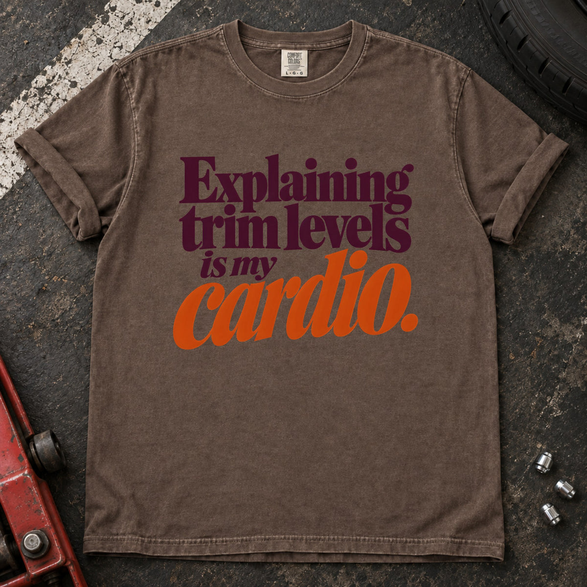 Espresso T-shirt with burgundy and orange lettering reading 'Explaining trim levels is my cardio'.