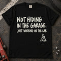 Black car enthusiast T-shirt. A jack stand backs not hiding in the garage, just working on the car.