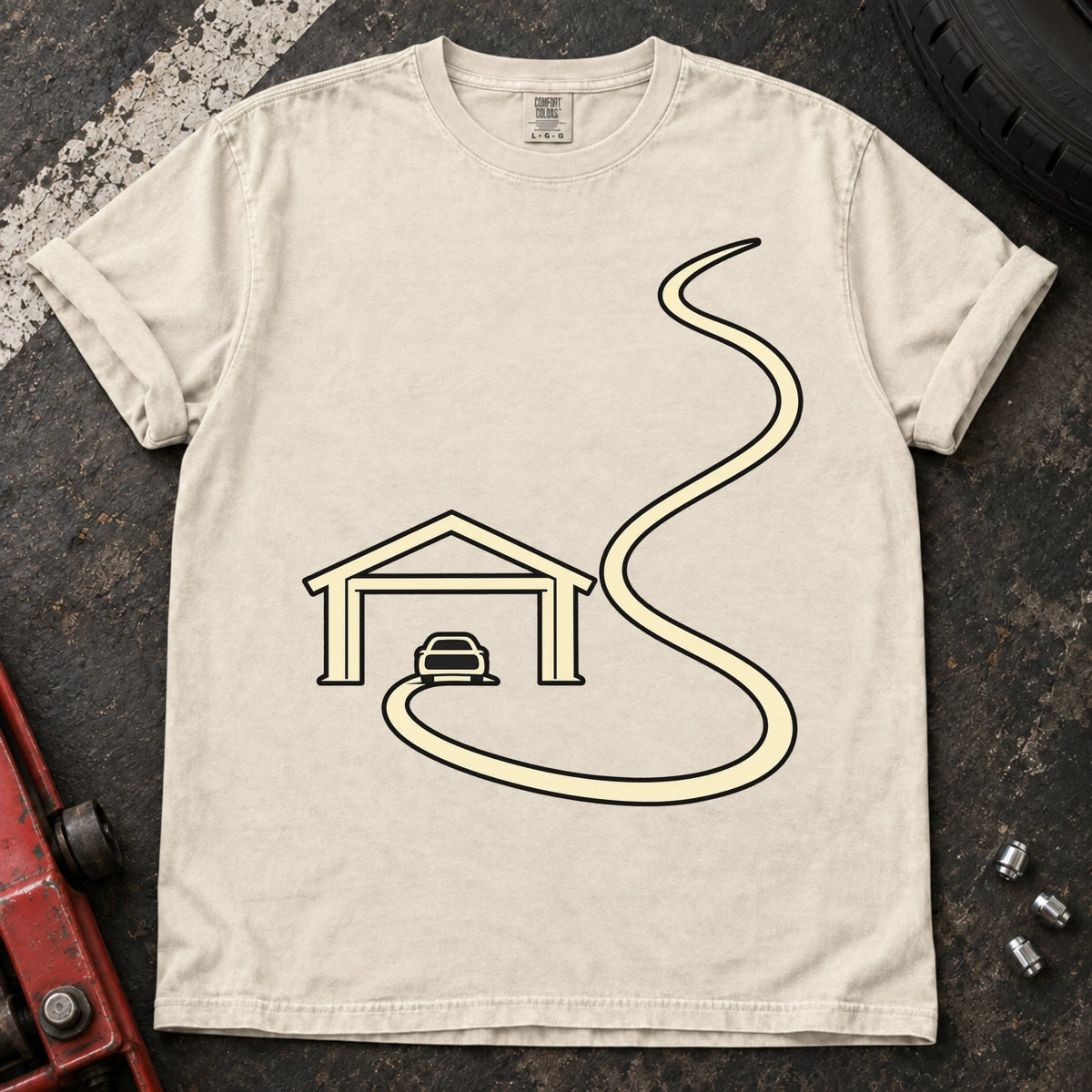 Ivory car enthusiast T-shirt. A minimal garage opens onto a long winding road.