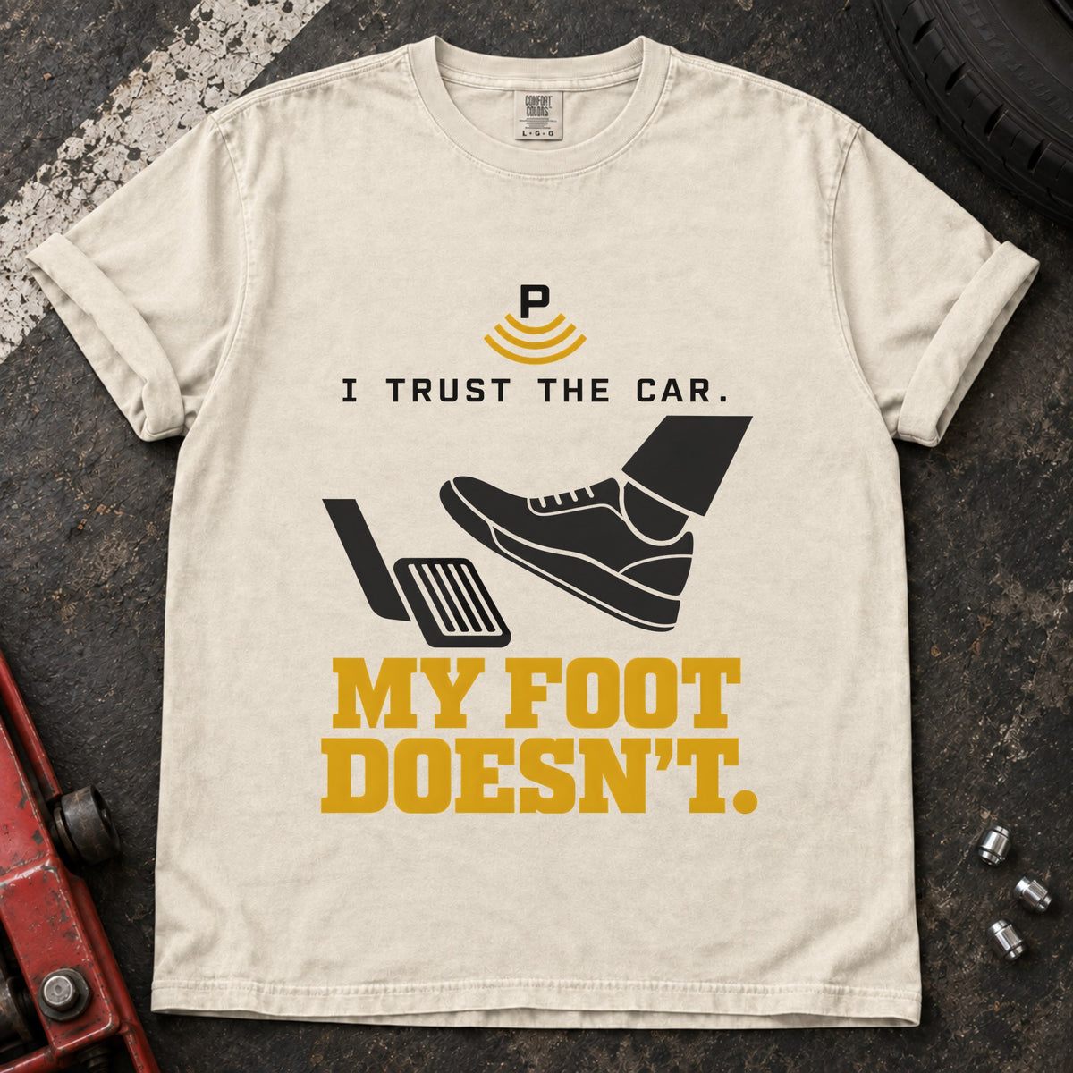 Ivory T-shirt showing a shoe near a pedal and a parking-assist symbol with 'I trust the car. My foot doesn't'.