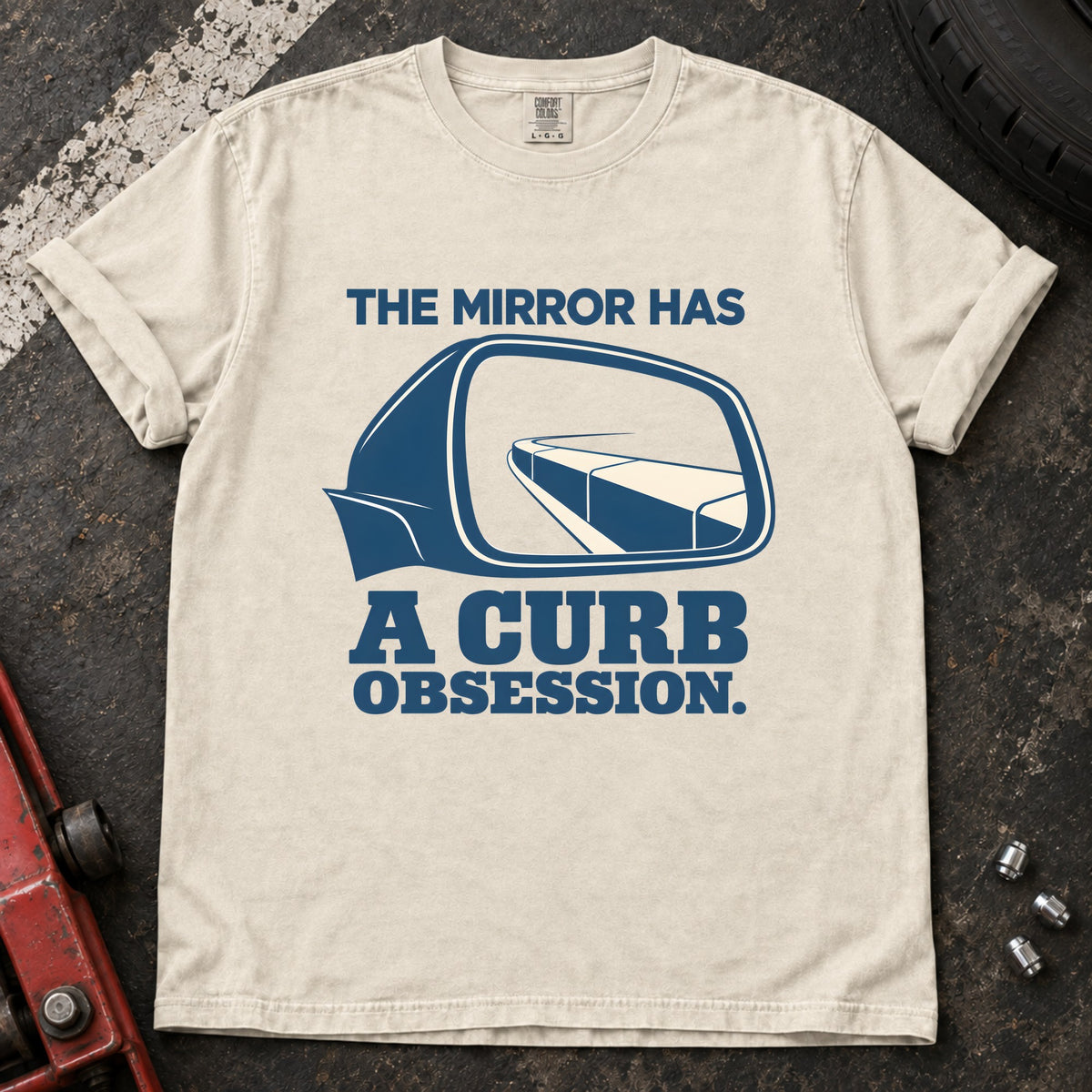 Ivory T-shirt showing a side mirror reflecting a curb with 'The mirror has a curb obsession'.