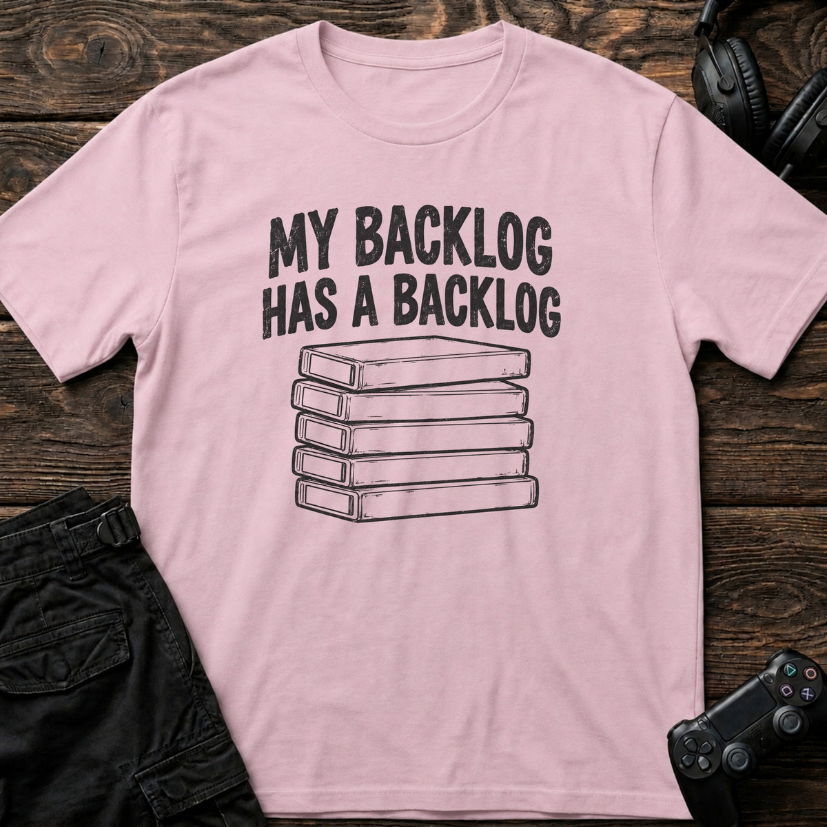 Light Pink gaming T-shirt. A stack of game cases illustrates my backlog has a backlog.