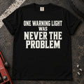 Black T-shirt with serif lettering reading 'One warning light was never the problem'.