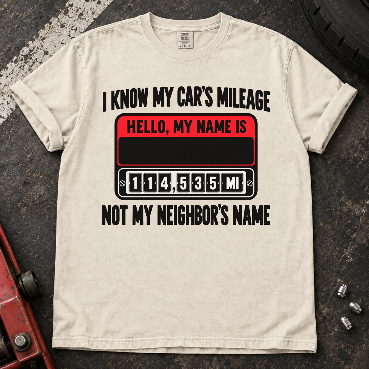 Ivory T-shirt showing a name badge and odometer with 'I know my car's mileage, not my neighbor's name'.