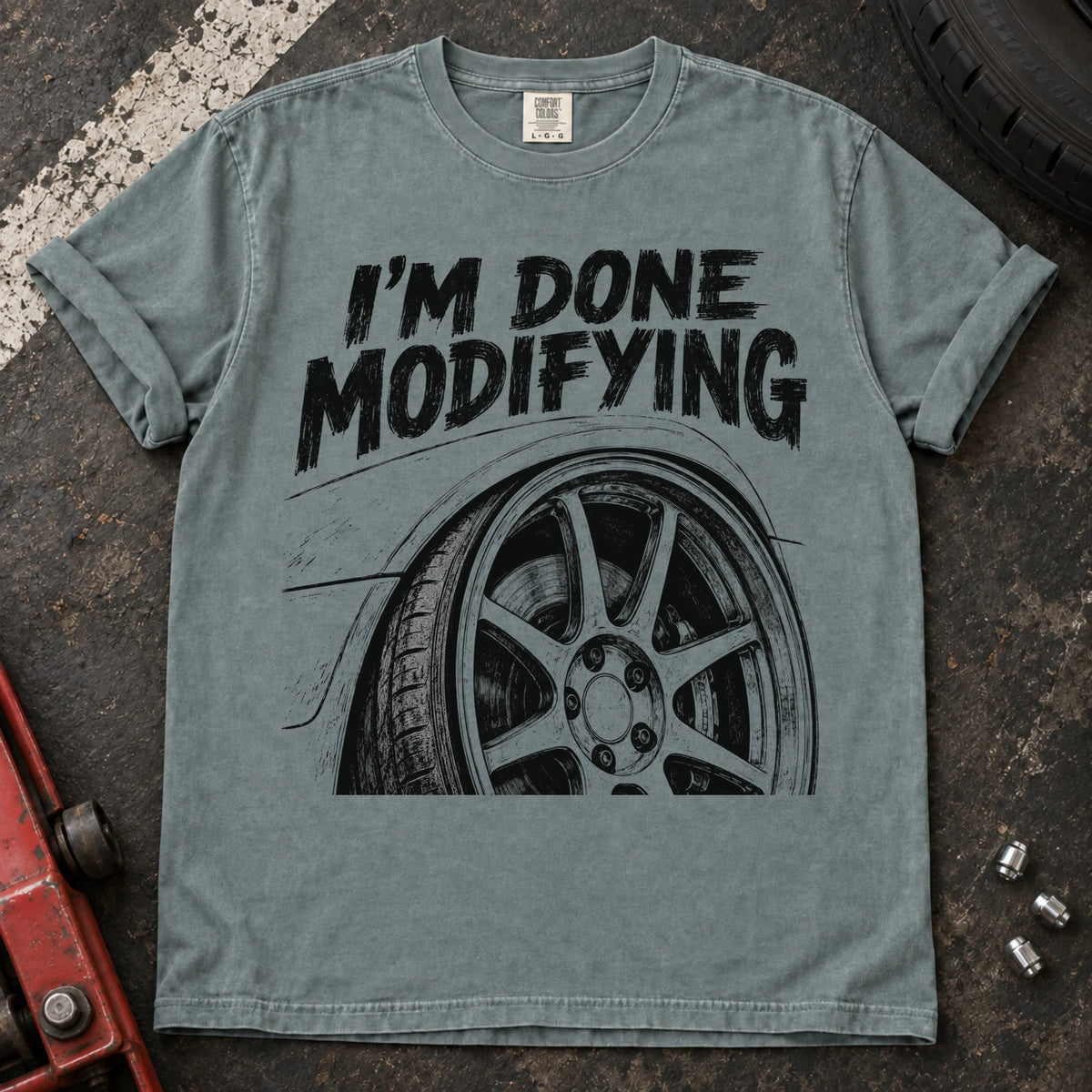 Bay car enthusiast T-shirt. A modified wheel sits under the familiar promise, I'm done modifying.