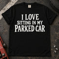 Black T-shirt with serif lettering reading 'I love sitting in my parked car'.