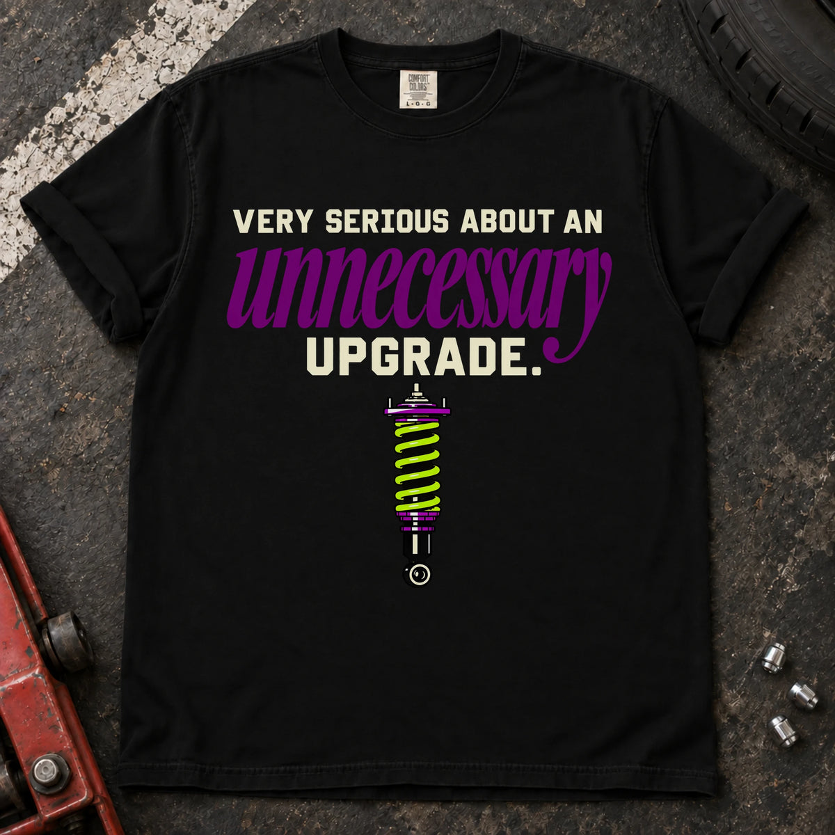 Black T-shirt showing a coilover beneath 'Very serious about an unnecessary upgrade' in cream and purple lettering.