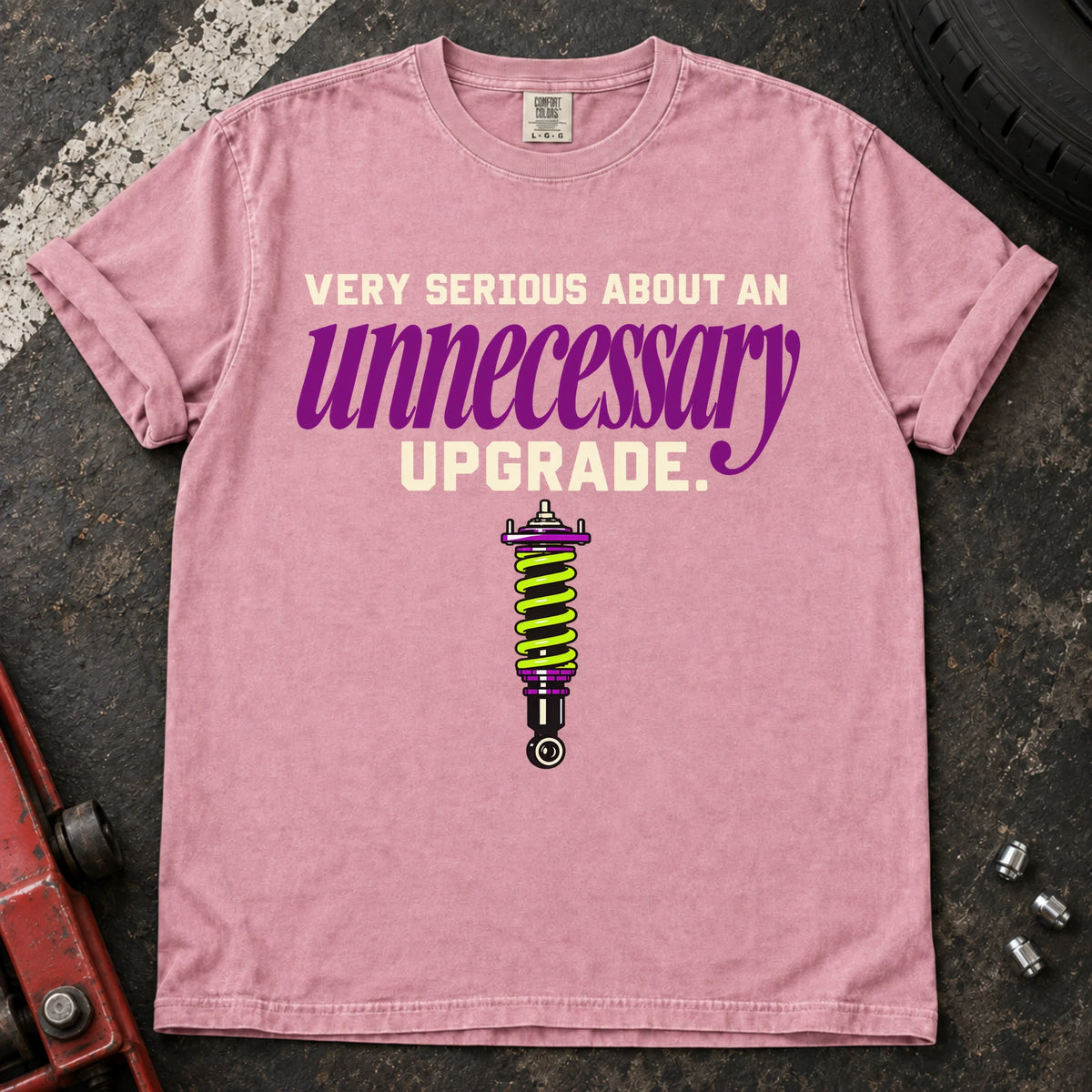 Blossom T-shirt showing a coilover beneath 'Very serious about an unnecessary upgrade' in cream and purple lettering.