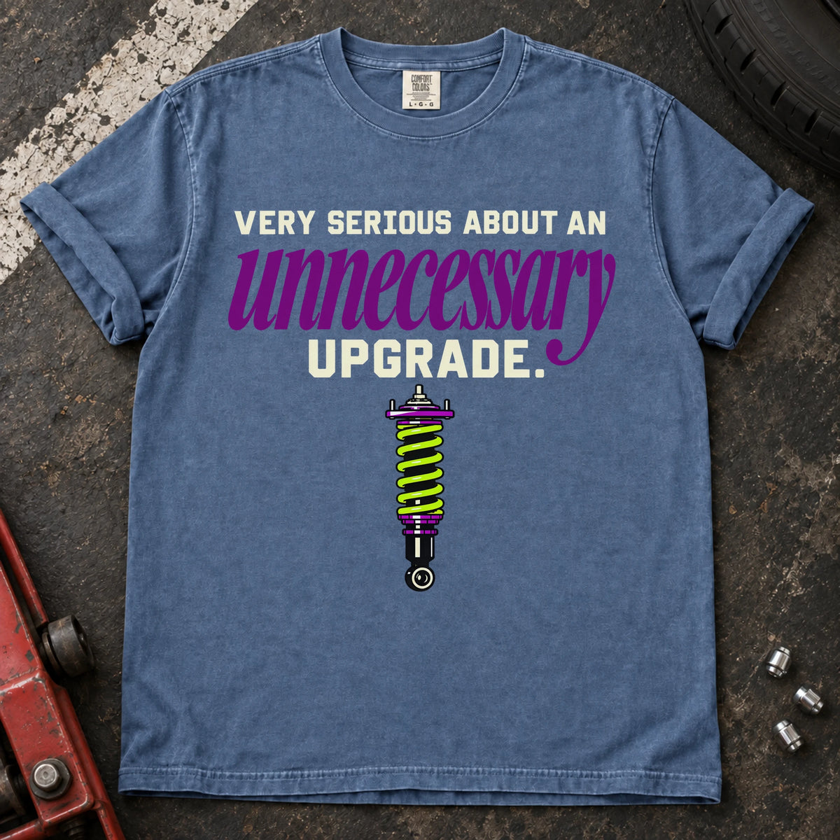 Blue Jean T-shirt showing a coilover beneath 'Very serious about an unnecessary upgrade' in cream and purple lettering.