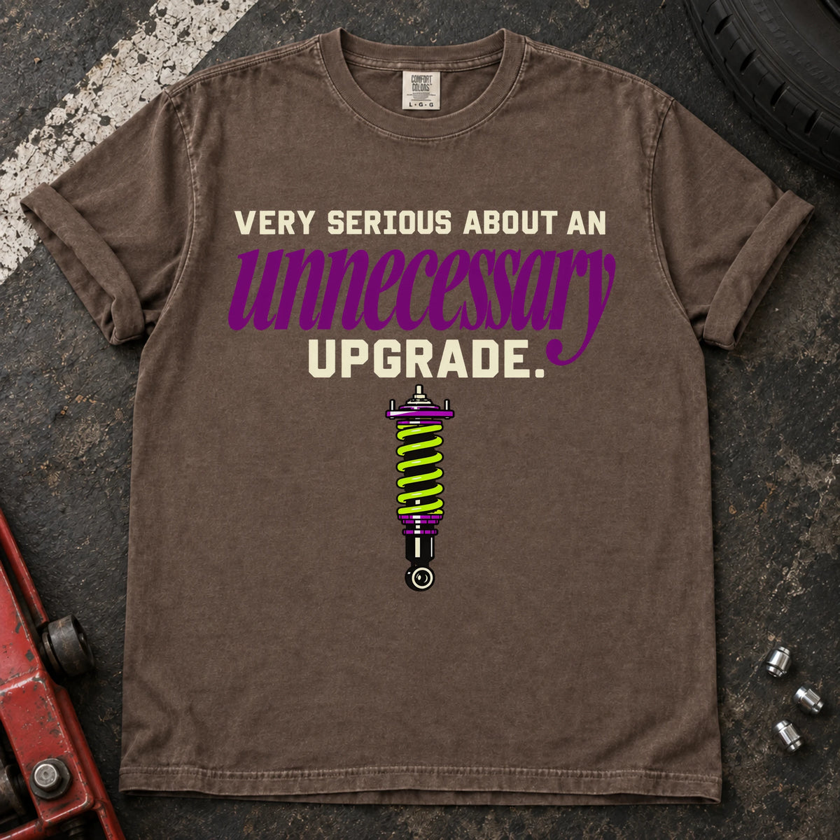 Espresso T-shirt showing a coilover beneath 'Very serious about an unnecessary upgrade' in cream and purple lettering.