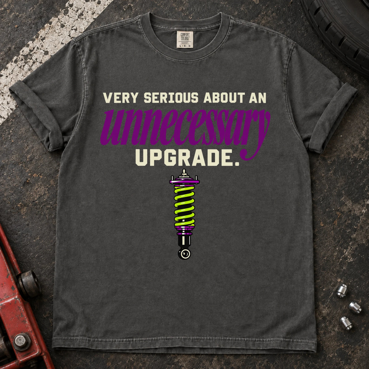 Pepper T-shirt showing a coilover beneath 'Very serious about an unnecessary upgrade' in cream and purple lettering.