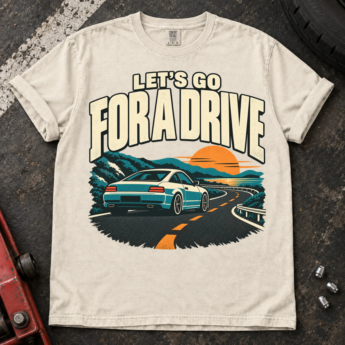 Ivory car enthusiast T-shirt. A car cruises a sunset mountain road under let's go for a drive.