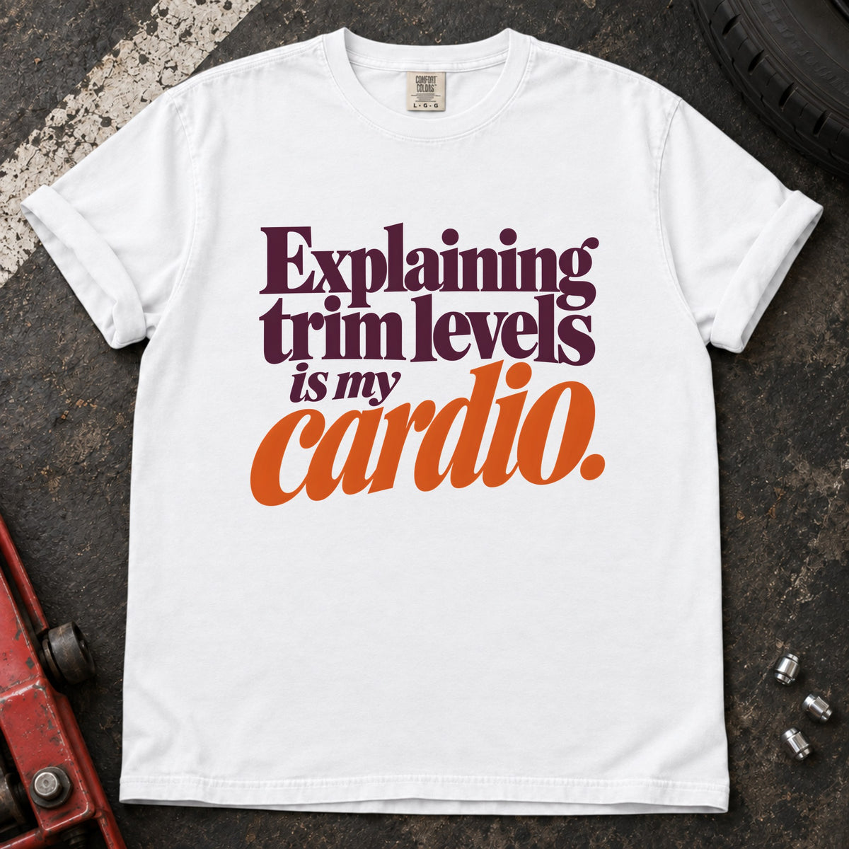 White T-shirt with burgundy and orange lettering reading 'Explaining trim levels is my cardio'.