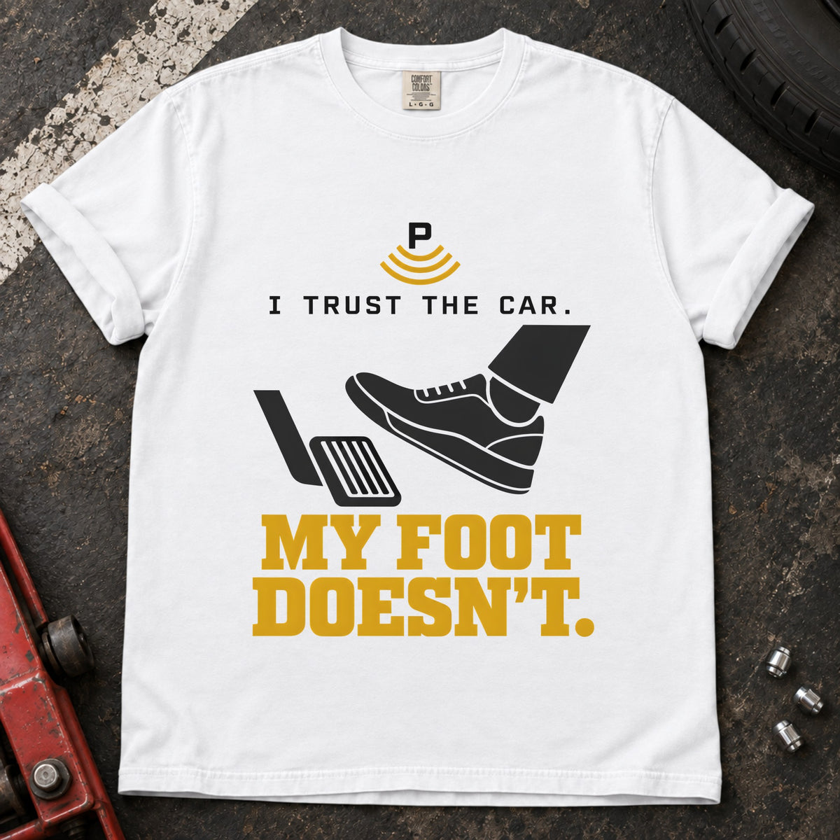 White T-shirt showing a shoe near a pedal and a parking-assist symbol with 'I trust the car. My foot doesn't'.